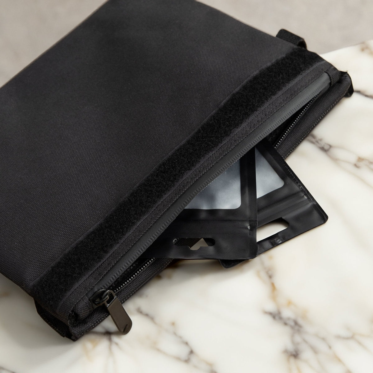 Close-up of a black Coast Angels Soho smell-proof pouch unzipped on a marble surface, revealing two sleek black resealable bags inside, highlighting discreet, functional storage.
